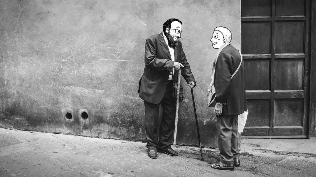Zwei alte Menschen auf einem Schwarz-Weiß-Foto an einer Mauer lehnend miteinander redend. Die Köpfe sind durch Zeichnungen der Köpfe von Nina Kiel und Marcus Richter ersetzt.